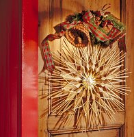 Straw star with Christmas decorations hanging to wooden door