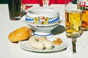 Two white sausages, bread and mustard sauce on plate with glass of beer