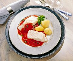 Ling fish fillet with tomato, coconut sauce and potatoes on plate