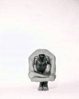 Woman with hair bun crouching and hiding her face between knees against white background