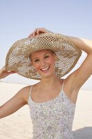 Portrait of happy woman wearing large straw hat on the beach, smiling broadly