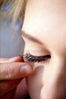 Close up: Frau klebt sich künstliche Wimpern ans geschlossene Auge