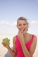 Portrait of blonde woman holding bunch of grapes and eating, smiling