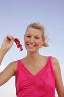 Blonde woman holding a branch of red currants in hand, smiling