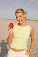 Woman holding a red apple standing on beach, laughing