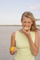 Blonde woman biting into slice of lemon and grimacing