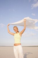 Portrait of beautiful woman in yellow top holding fluttering cloth on beach, smiling