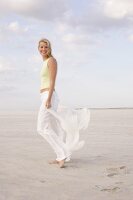 Portrait of beautiful woman holding scarf and walking on beach, smiling