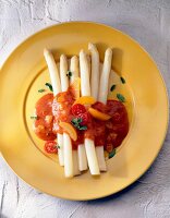 Asparagus with tomato and apricot sauce on yellow plate, overhead view