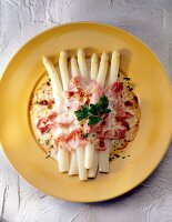 Asparagus garnished with cheese cream sauce and ham on yellow plate