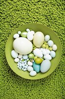 Grüne Schale auf grünem Teppich mit vielen verschiedenen Eiern darin