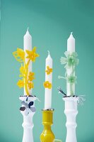 Close-up of three candlesticks decorated with wax flowers against turquoise background