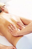 Woman receiving massage on her lower back from masseur with flat hands, relaxing