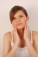 Portrait of pretty woman with brown hair massaging her face with hands