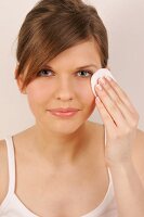 Portrait of gray eyed Magdalena woman with brown hair cleaning her under eye with pad