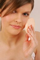 Close-up of gray eyed Magdalena woman with brown hair applying make-up with a sponge