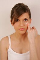 Portrait of pretty woman with brown hair applying cream below her eye with finger