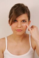 Portrait of pretty woman with brown hair applying cream below her eye with finger