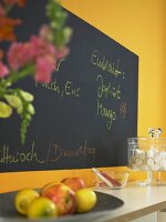 Fruit bowl and marshmallows in glass jar on table in front of orange wall with chalkboard