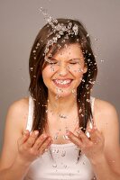 Frau mit braunen Haaren reinigt Gesicht mit Wasser