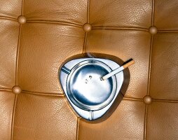 Close-up of burning cigar in silver ashtray against brown leather background