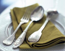 Silver fork and spoon on green napkin and white plate