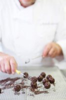 Close-up of chef rolling chocolate truffles on grid