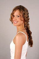 Portrait of cheerful brown haired young woman with braid wearing a white top, smiling