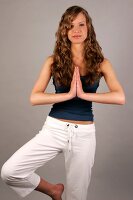Beautiful woman with long curly hair wearing blue top performing yoga, smiling