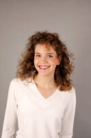 Portrait of beautiful woman with curly hair wearing white sweater, smiling widely