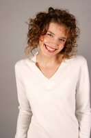 Portrait of beautiful woman with curly hair wearing white sweater, smiling widely