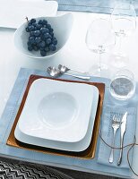 Table setting with white and copper square plates on light blue table cloth