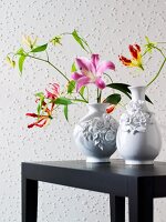 Two floral designed vase with fresh flowers on table against beaded wall