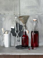 Stillleben mit Kirsch-Vanillesirup in Flaschen & Küchenutensilien