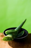 Close-up of bowl with aloe vera branch kept on wooden table against green background