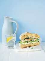 A fish burger with cucumber and a glass of water