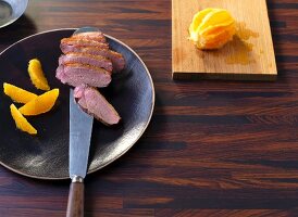 Sliced duck breast fillets being arranged on a plate with orange fillets