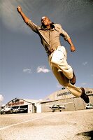 Man in formals jumping in air with an outstretched arm on airfield