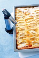 Close-up of kitchen torch being used to caramelize apple pie with cream