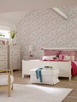Weisses Doppelbett und Kommode im Schlafzimmer mit rosa-weiß geblümter Tapete und Dachbalken