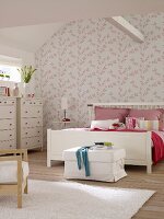 White double bed and chests of drawers in bedroom with pink and white floral wallpaper and ceiling beam