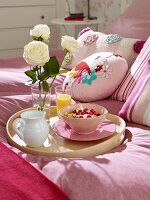 Breakfast tray with muesli, orange juice and roses on pink bed