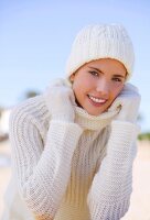 Portrait of pretty woman wearing white woolly sweater, hat and gloves in winter, smiling