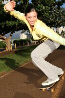 Schwarzhaarige Frau im gelben Pulli auf einem Skateboard