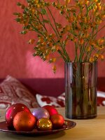 Rose hip branches in vase and baubles in bowl in front