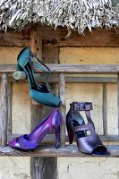 Close-up of dark green satin pumps, purple strappy pumps and peep toe on wooden surface