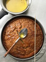 Spoon of orange syrup over baked cake in baking tray