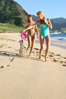 Two women running along the beach with a dog