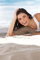 Portrait of ecstatic woman lying on sand with head propped on hand, laughing