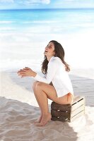 Portrait of woman with dark hair wearing white jacket sitting on wooden crate at beach